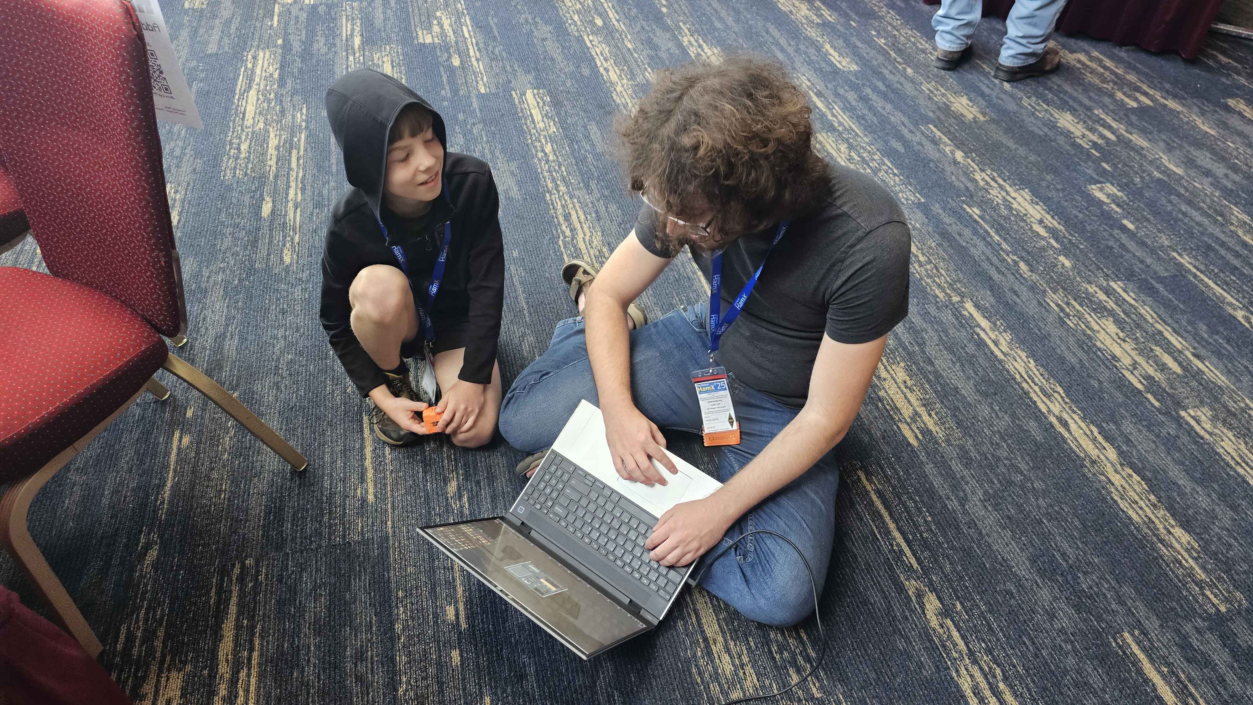 Developer Lucas W1BTR sitting on the convention floor demonstrating Radiocraft on a laptop to a young attendee